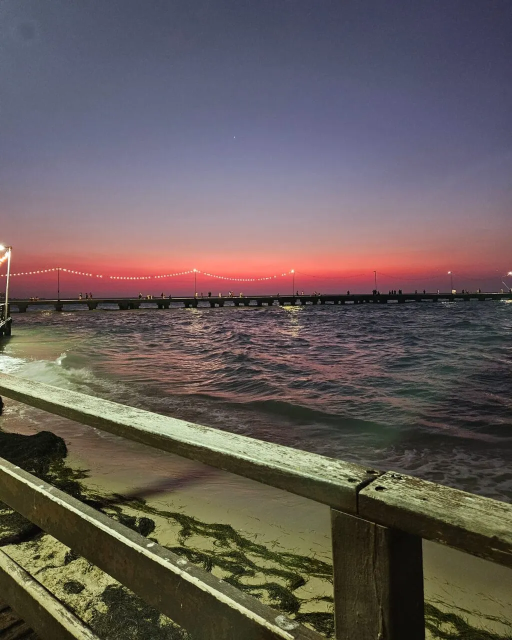 A pier stretching out over the Gulf at dusk, its lights strung against a red horizon.